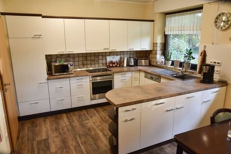 Eine Küche mit weißen Schränken, Holzböden, Geräten aus Edelstahl und einem Tisch.