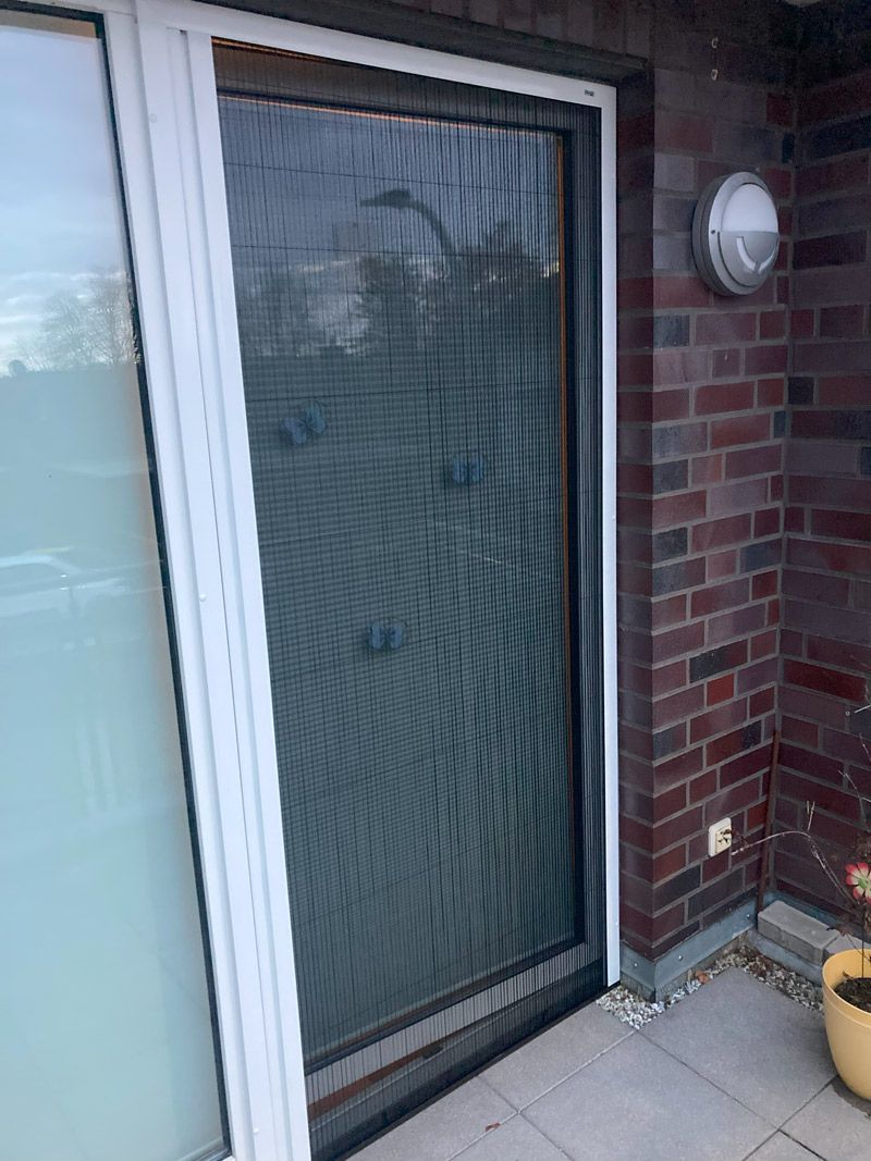 Auf einer Terrasse neben einer Backsteinmauer befindet sich eine Glasschiebetür mit einem Fliegengitter.
