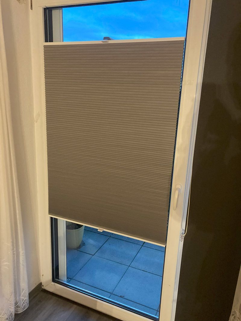 Ein Fenster mit Jalousien führt auf einen Balkon.