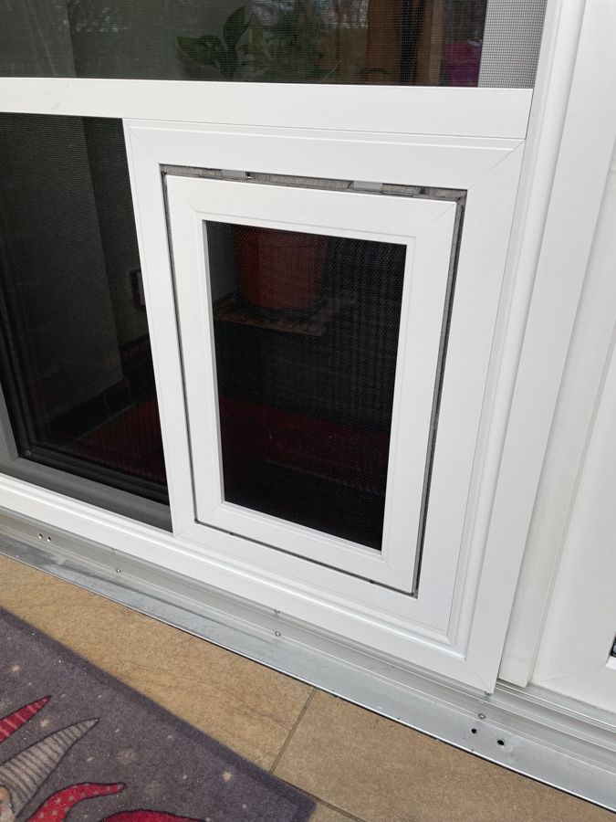 Eine weiße Glasschiebetür mit eingebauter Hundeklappe.