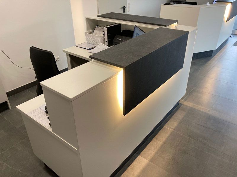 Ein weiß-schwarzer Rezeptionstresen mit einem Laptop darauf.