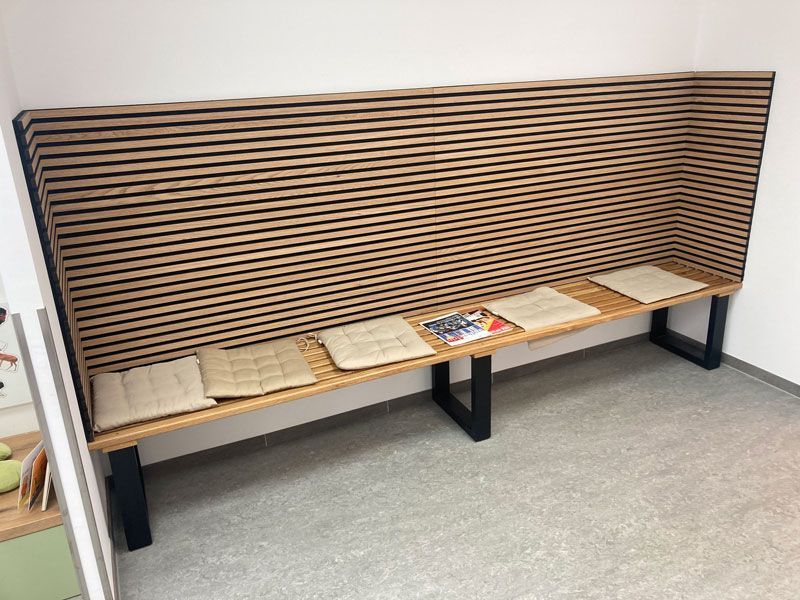 In einem Wartezimmer steht eine lange Holzbank.