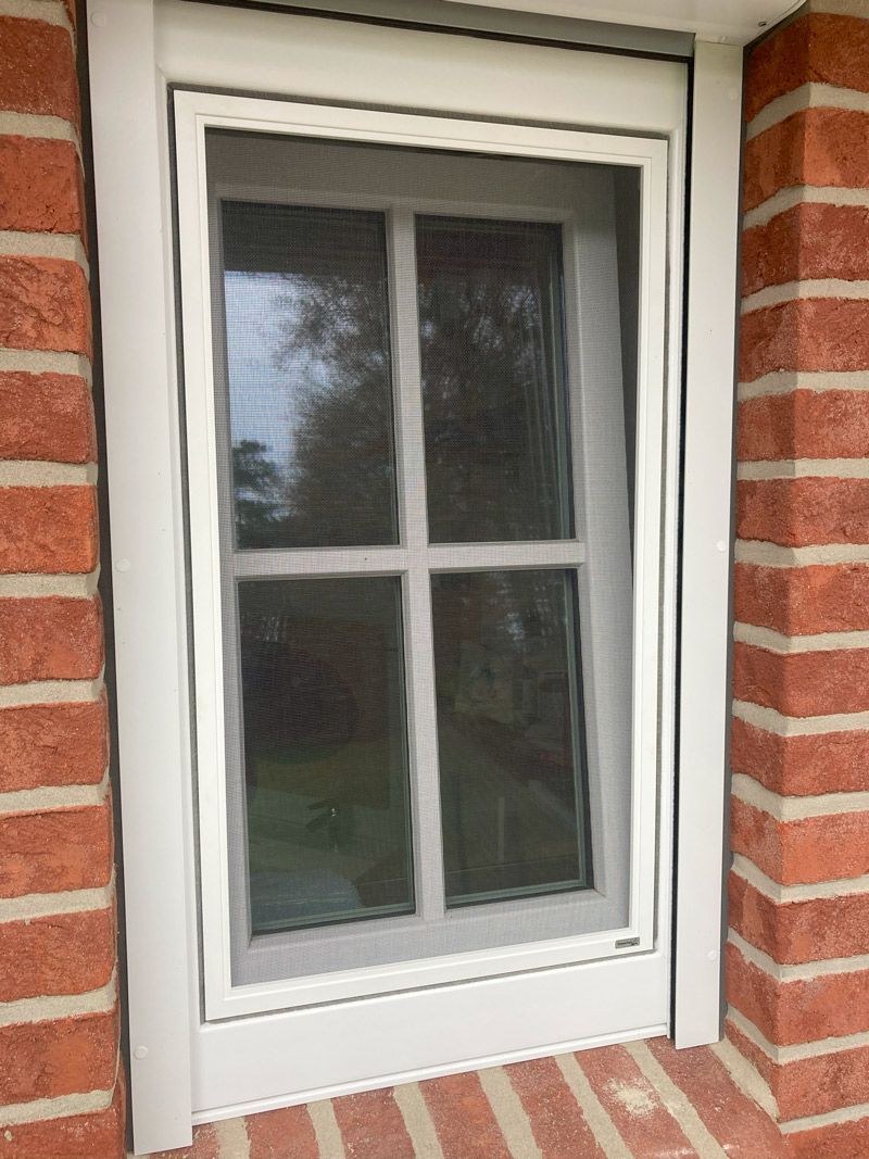 In einer Ziegelwand befindet sich ein weißes Fenster mit einem Fliegengitter.