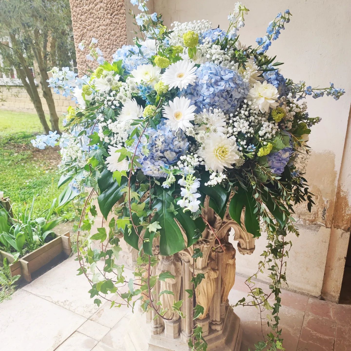 Grand arrangement floral blanc et bleu dans une jardinière décorative, sur une terrasse.