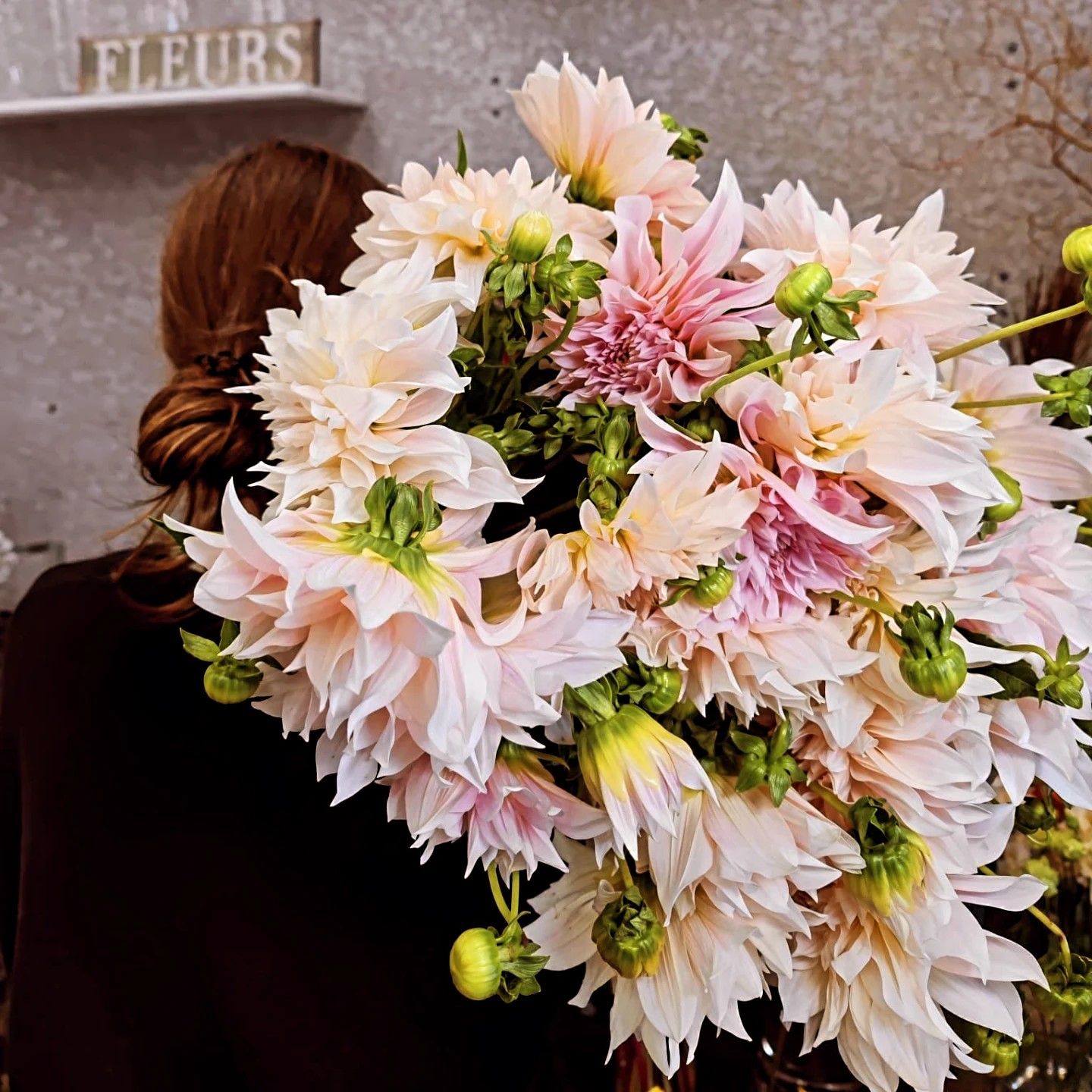 Une femme tenant un grand bouquet de dahlias dans une boutique.