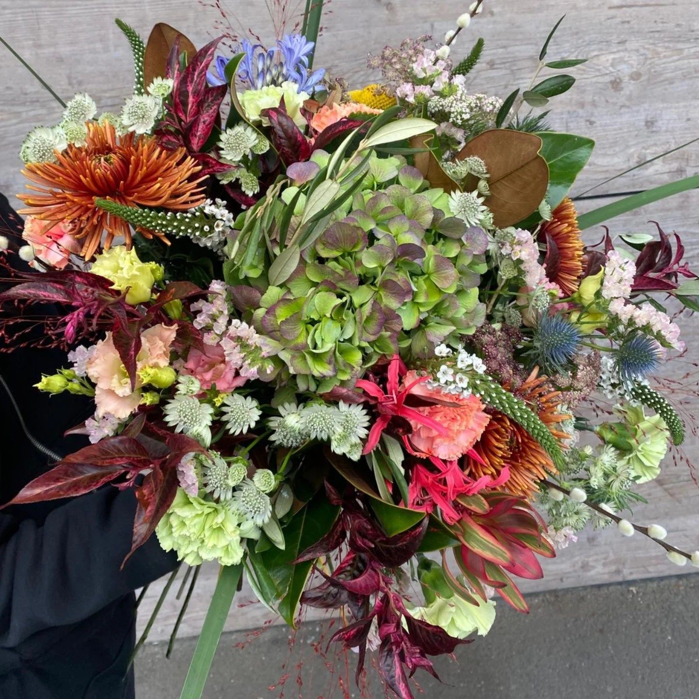 Bouquet varié de fleurs colorées et de verdure suspendu au-dessus d'une terrasse en bois.