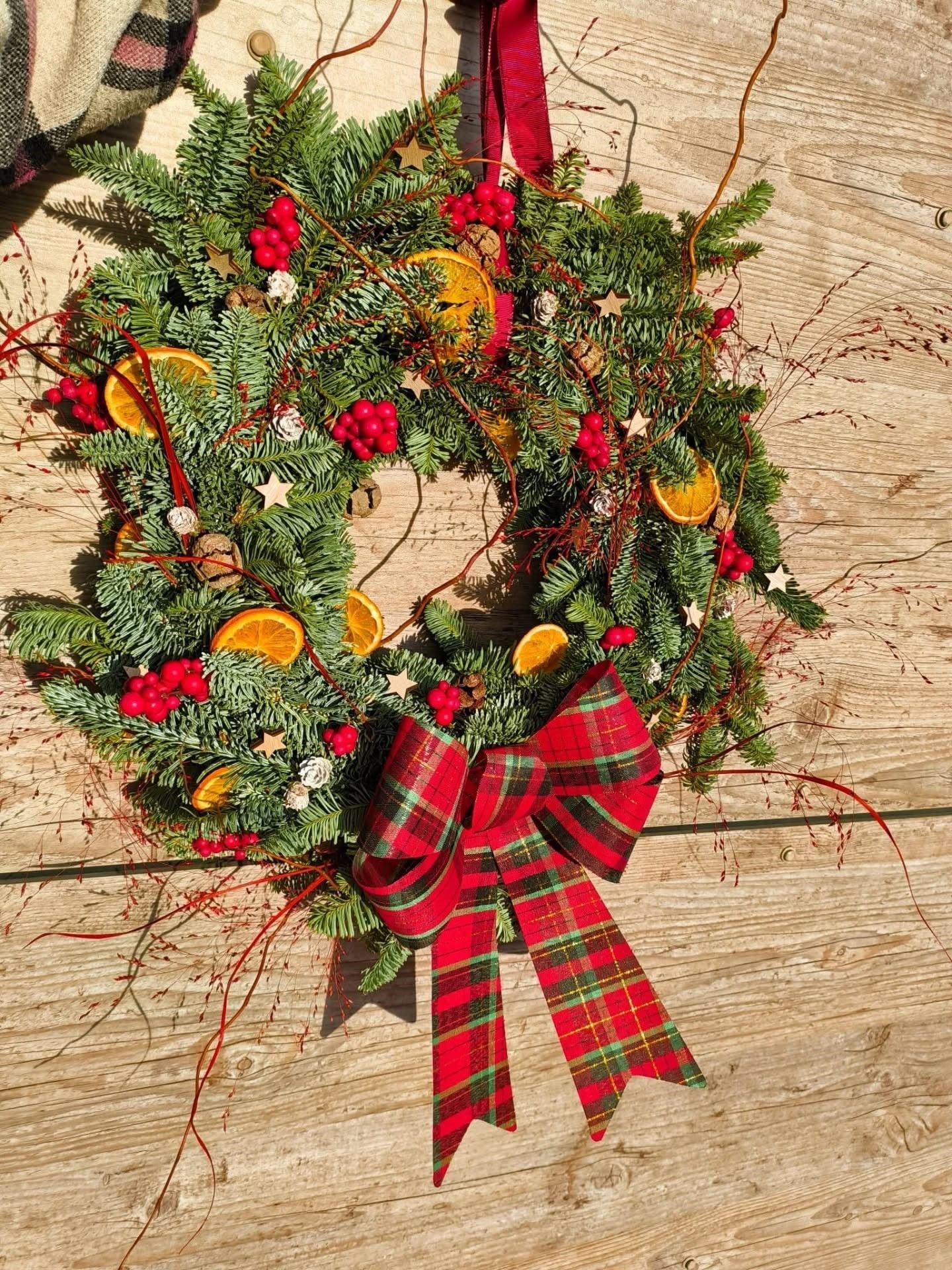 Couronne de Noël avec un nœud à carreaux rouges, des décorations et des tranches d'orange séchées sur un mur.