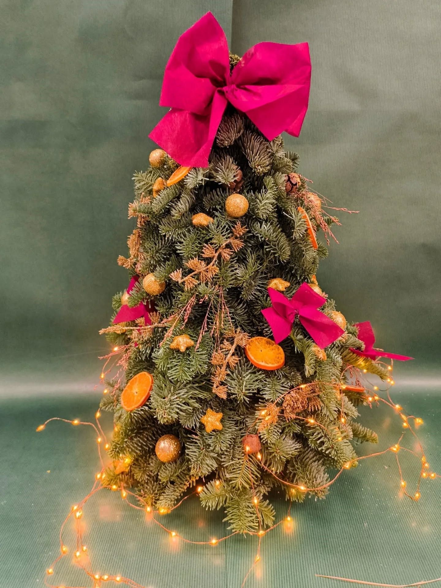 Sapin de Noël décoré de nœuds roses, de boules orange et de lumières blanches.