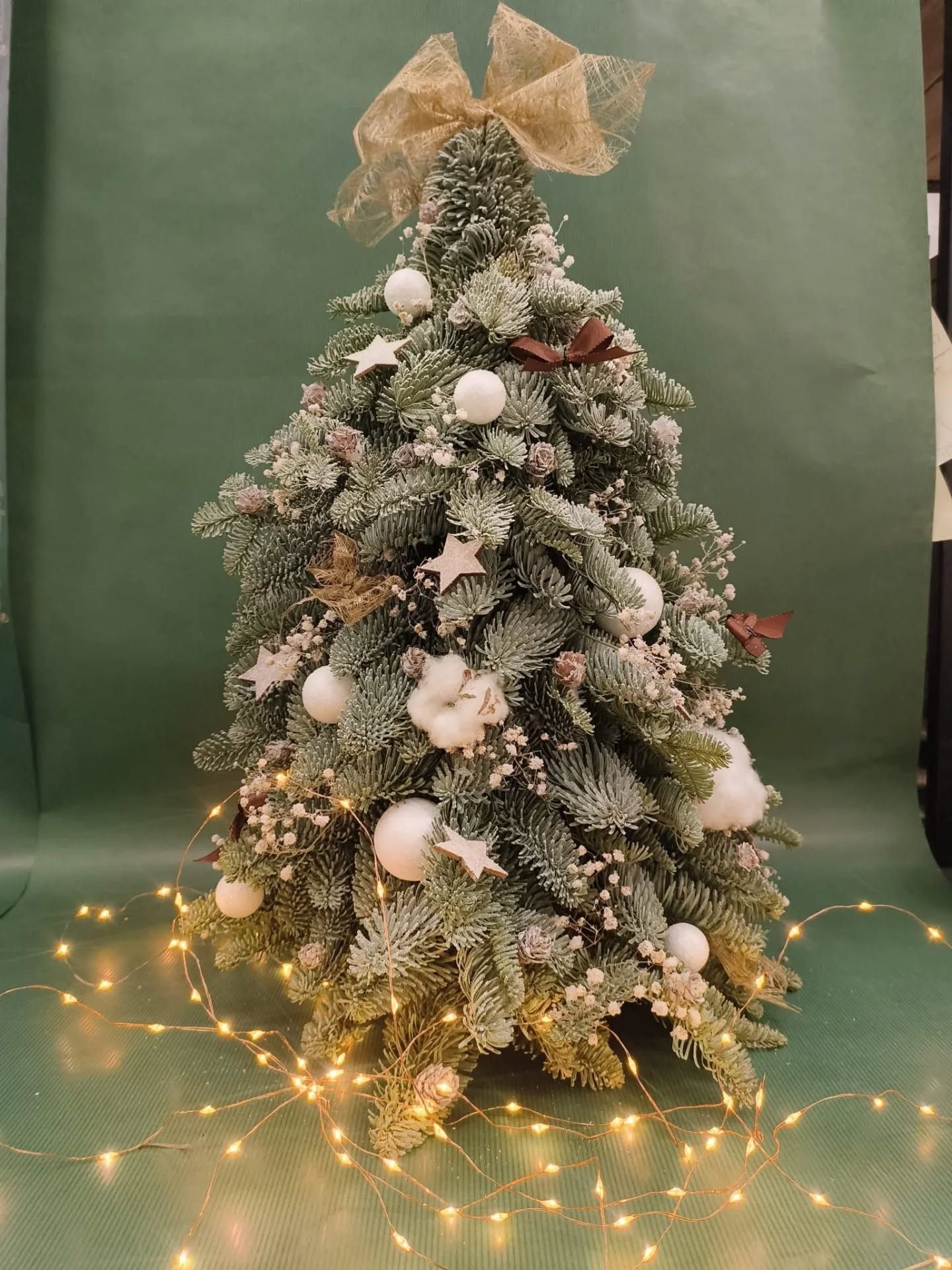 Sapin de Noël enneigé orné de décorations blanches, d'une étoile dorée à sa cime et de guirlandes lumineuses aux tons chauds.