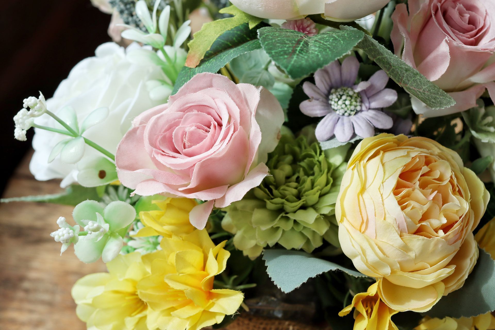 Bouquet de roses pastel, de fleurs blanches et de fleurs jaunes avec du feuillage vert.