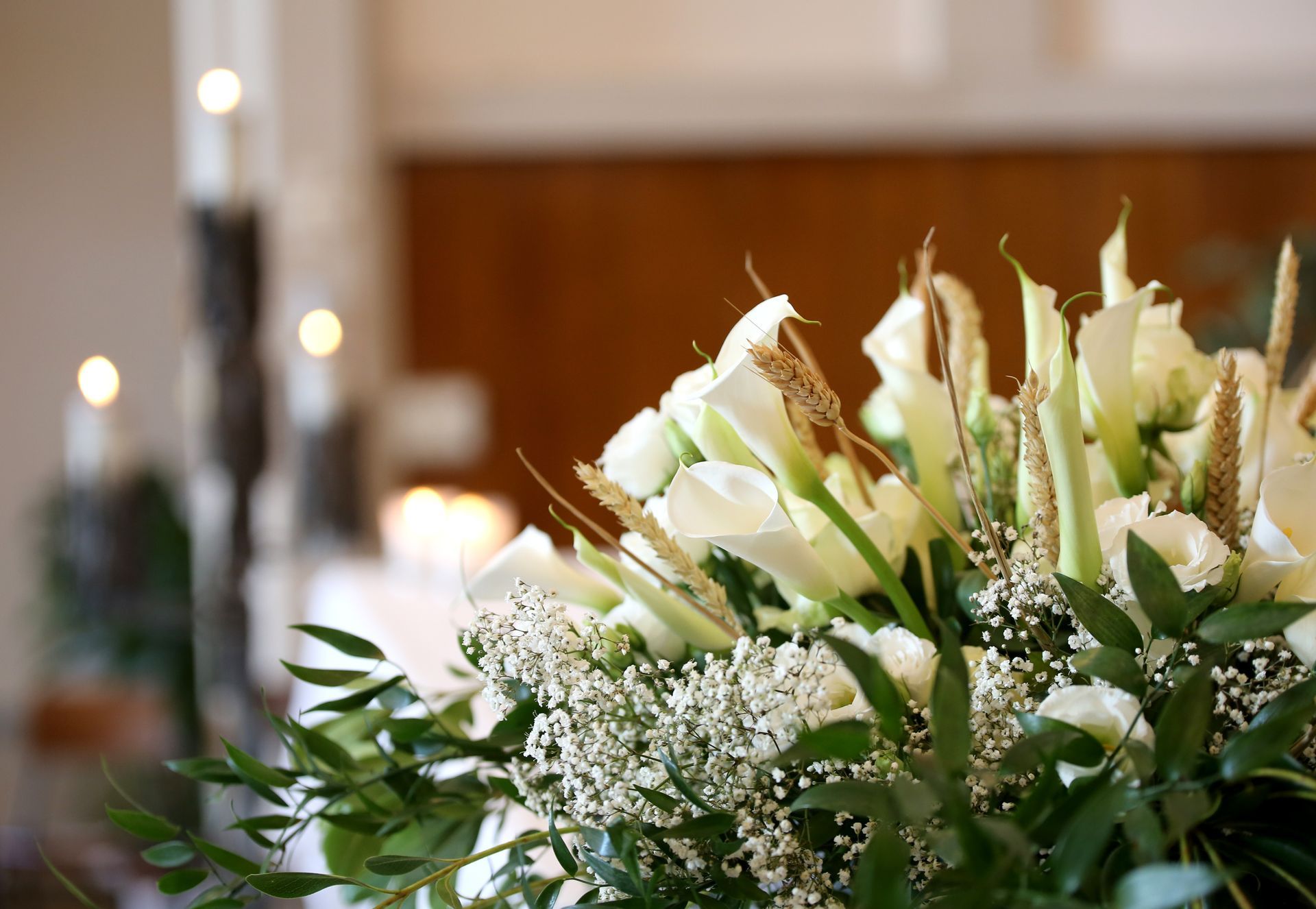 Composition florale blanche avec des lys et de la gypsophile sur une table dans un intérieur à l'éclairage tamisé.
