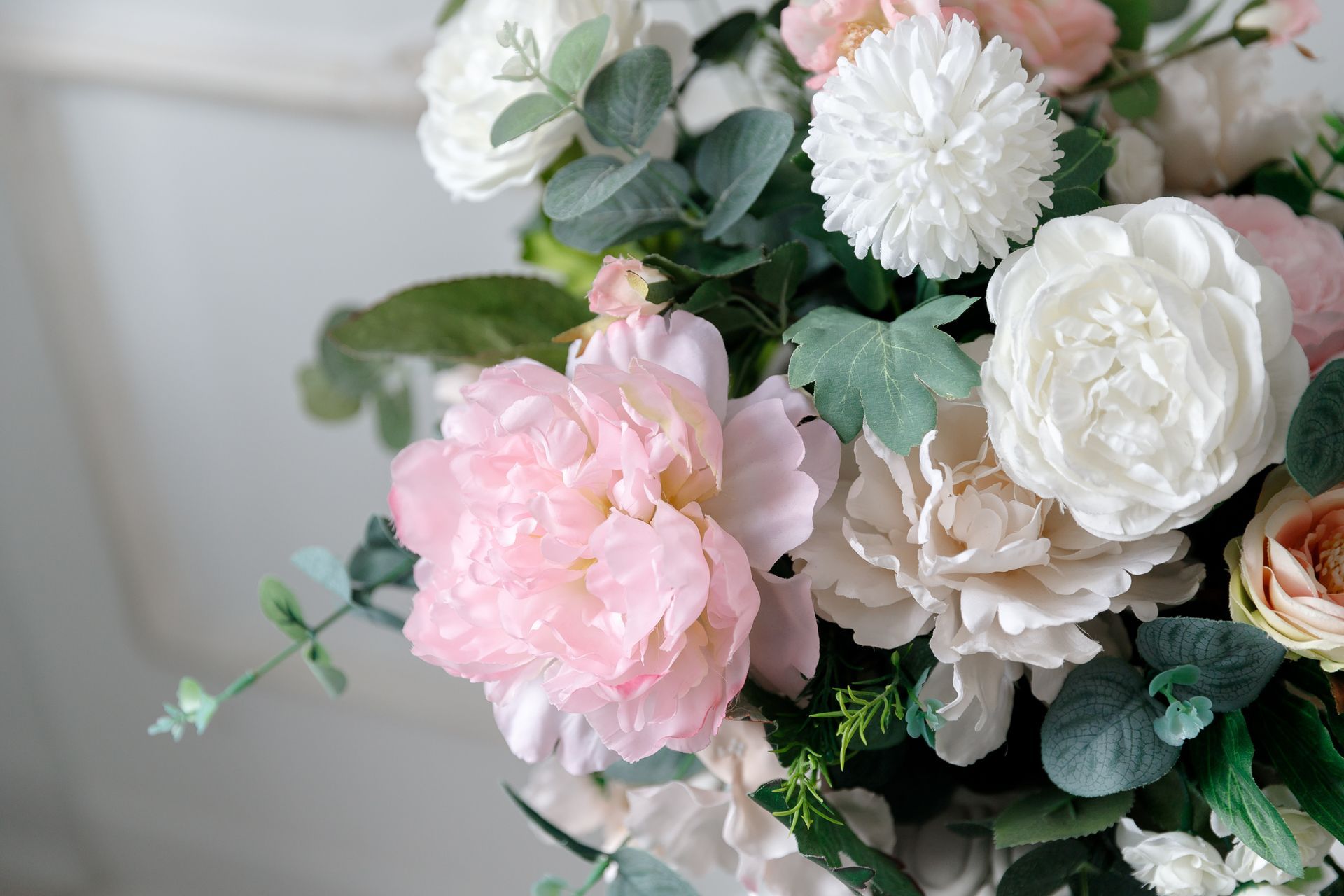 Bouquet de fleurs blanches, roses et crème avec des feuilles vertes sur un fond doux.