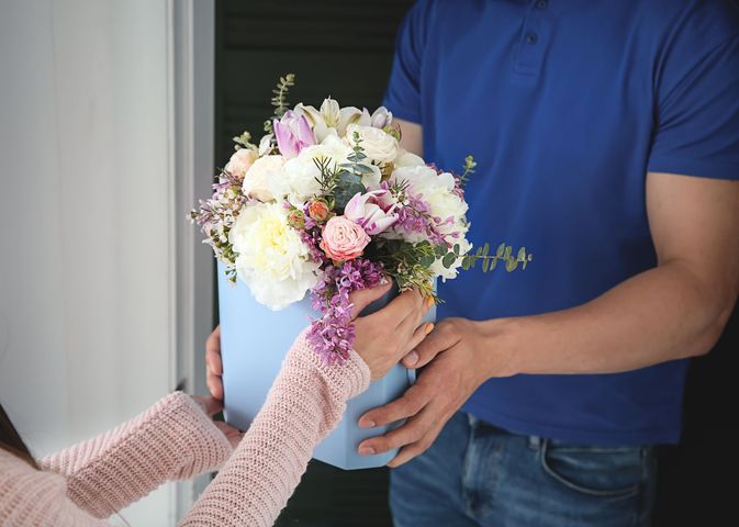 Une femme reçoit un bouquet de fleurs, remis par un livreur au tee-shirt bleu.