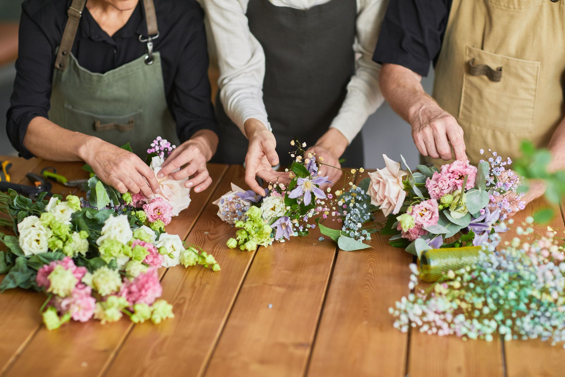 Trois personnes préparent des bouquets champêtres aux tons pastel.