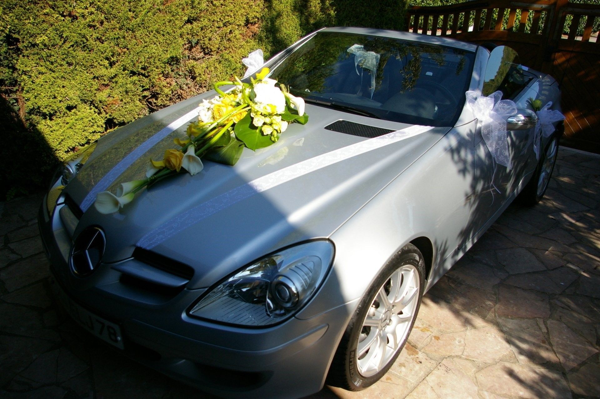Cabriolet argenté avec des fleurs sur le capot, garé à l'extérieur au soleil.