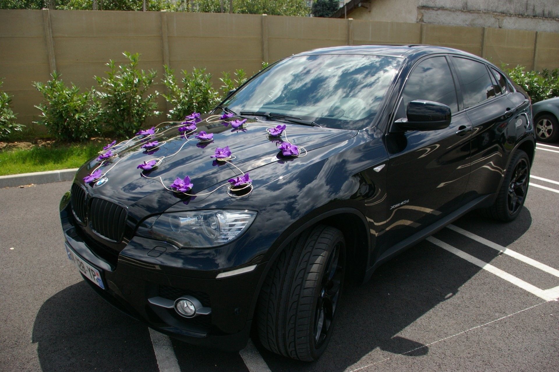 Une berline noire ornée de fleurs violettes, garée sur un parking près d'une clôture.