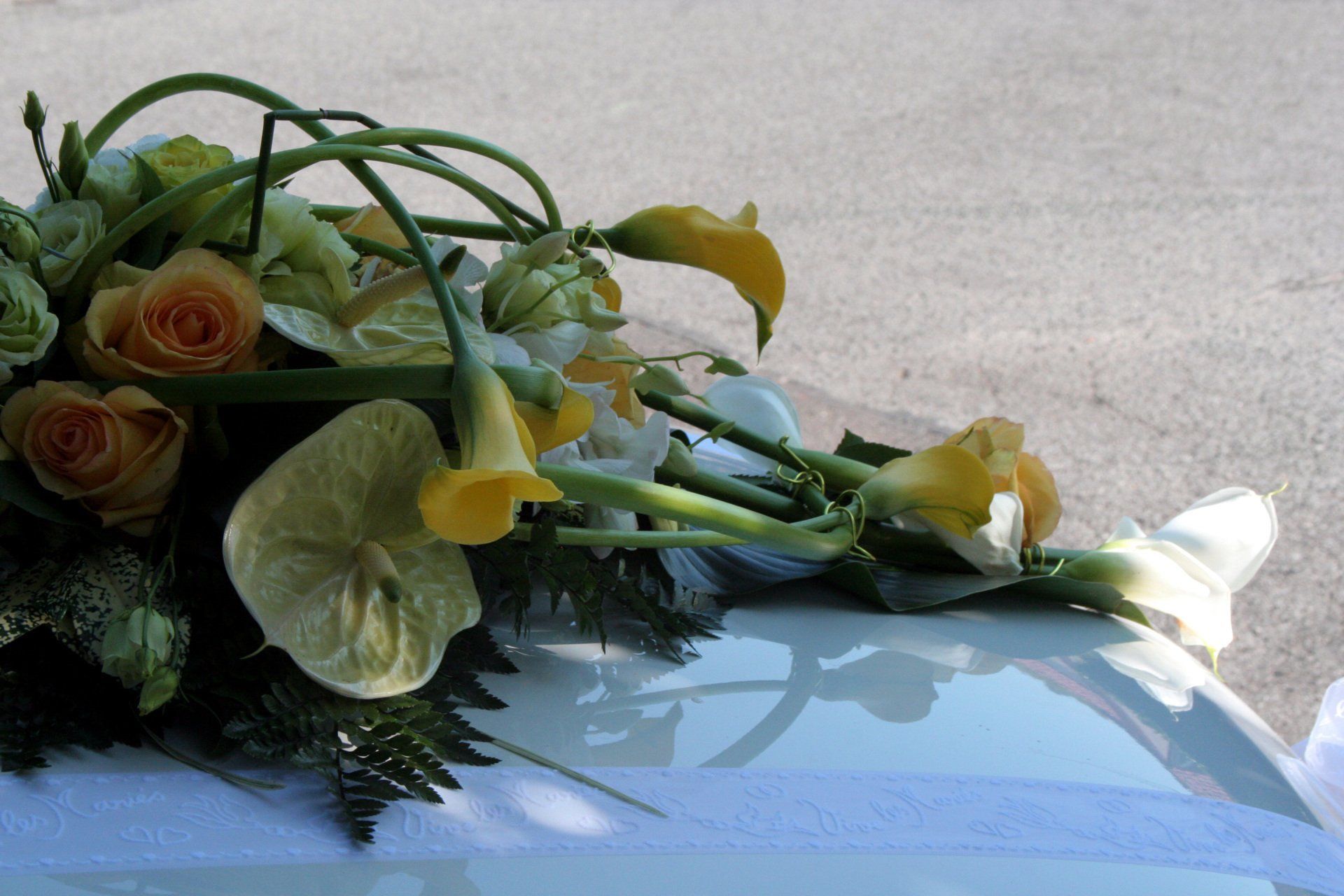 Bouquet de fleurs blanches et jaunes posé sur le capot d'une voiture bleu clair au soleil.