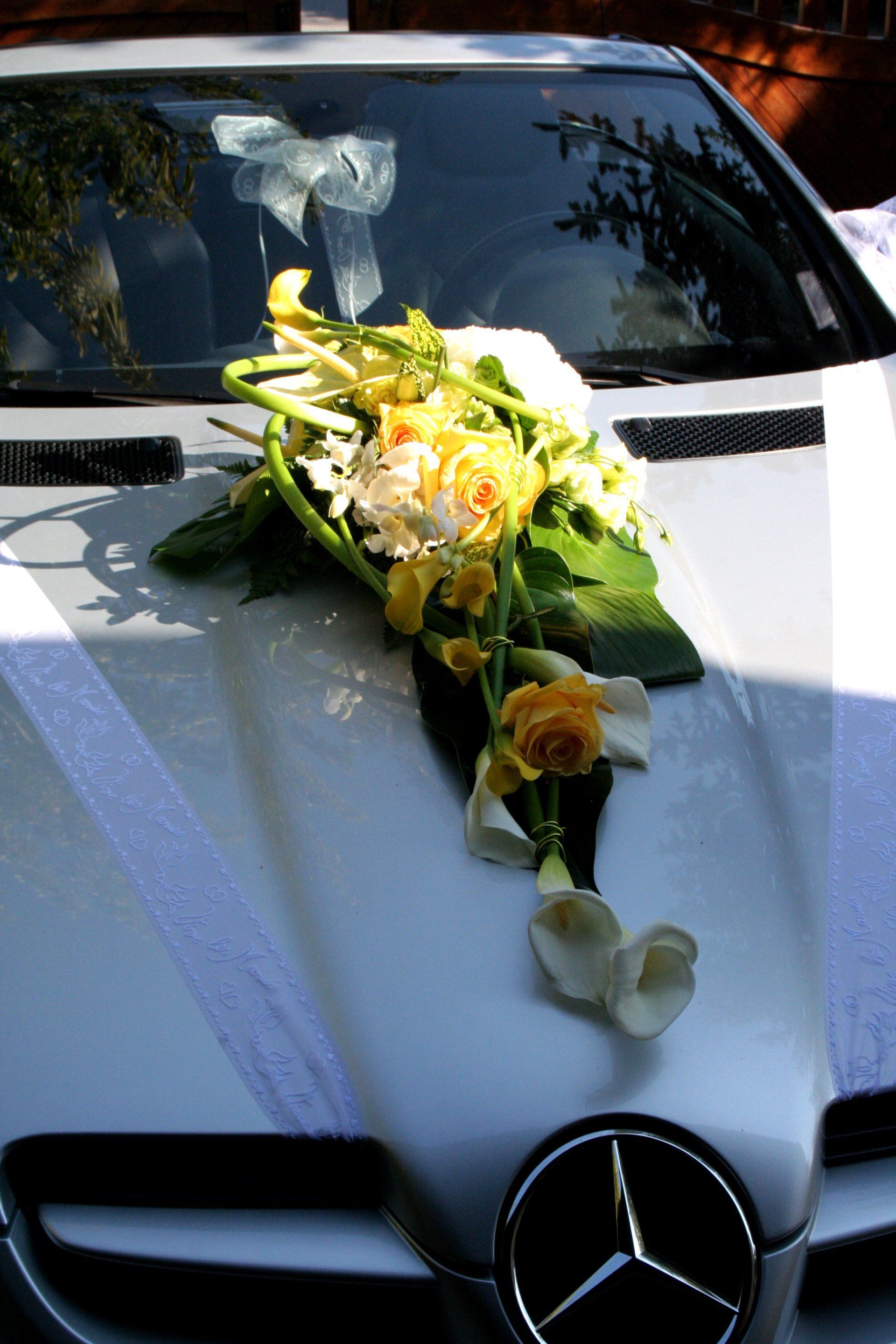 Capot de Mercedes blanche orné d'un bouquet de fleurs de mariage en cascade et d'un ruban à l'avant.