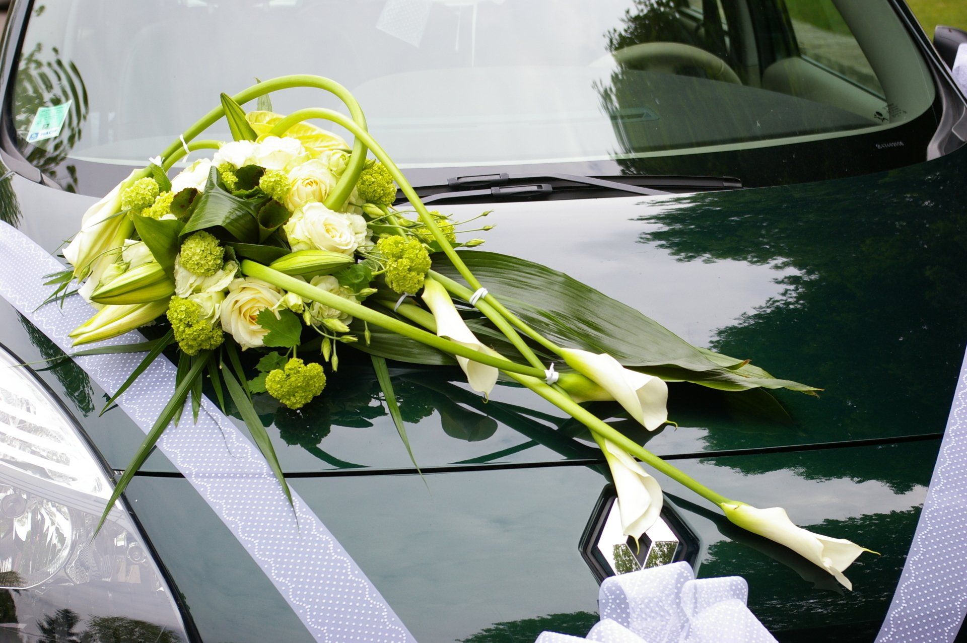 Composition florale posée sur un capot de voiture orné d'un ruban blanc.