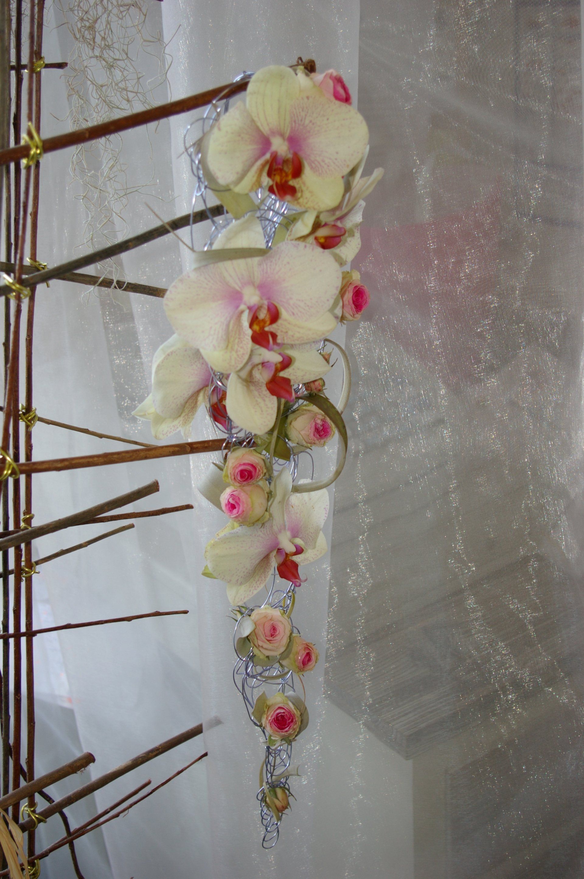Composition d'orchidées blanches à cœur rose sur de hautes tiges, devant un rideau transparent et satiné.