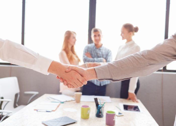 Deux individus qui se serrent la main devant un groupe de trois personnes