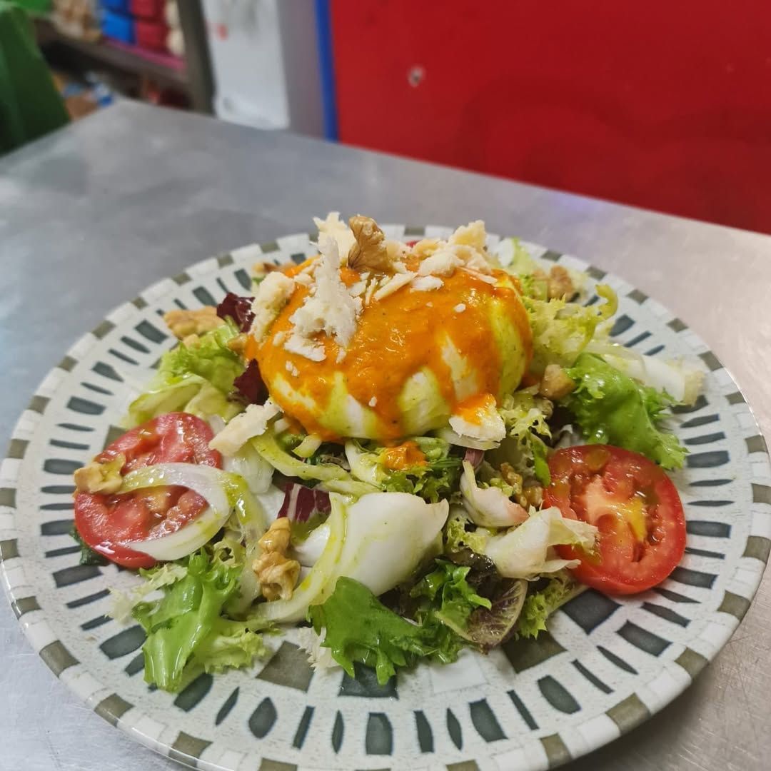 Ensalada con huevo escalfado, tomates, lechuga y aderezo en un plato decorativo.