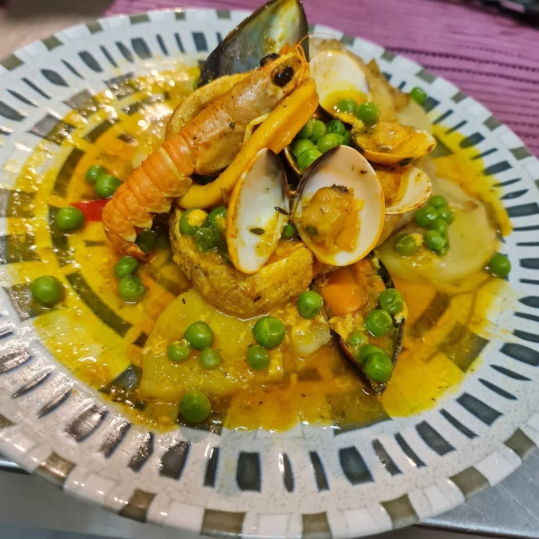 Guiso de mariscos con camarones, almejas, mejillones, guisantes y patatas en un caldo amarillo sobre un plato estampado.