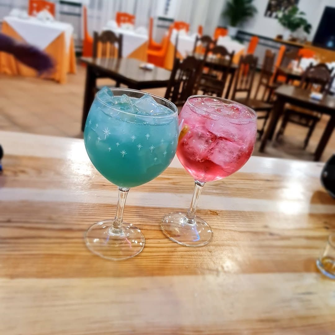Dos cócteles coloridos sobre una mesa de madera en un restaurante. Uno azul y el otro rosa.