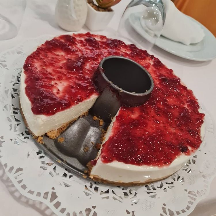 Tarta de queso con cobertura roja sobre un tapete de papel decorativo, al que le falta un trozo.