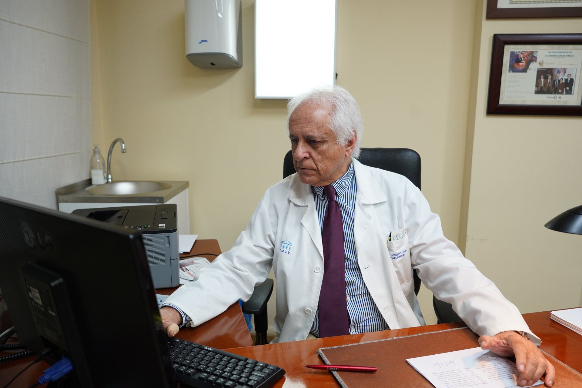 Un médico con bata blanca se sienta en una sala de exámenes con equipo médico.