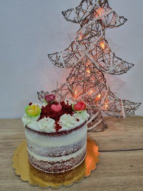 Un pastel de terciopelo rojo está sobre una mesa de madera frente a un árbol de Navidad.