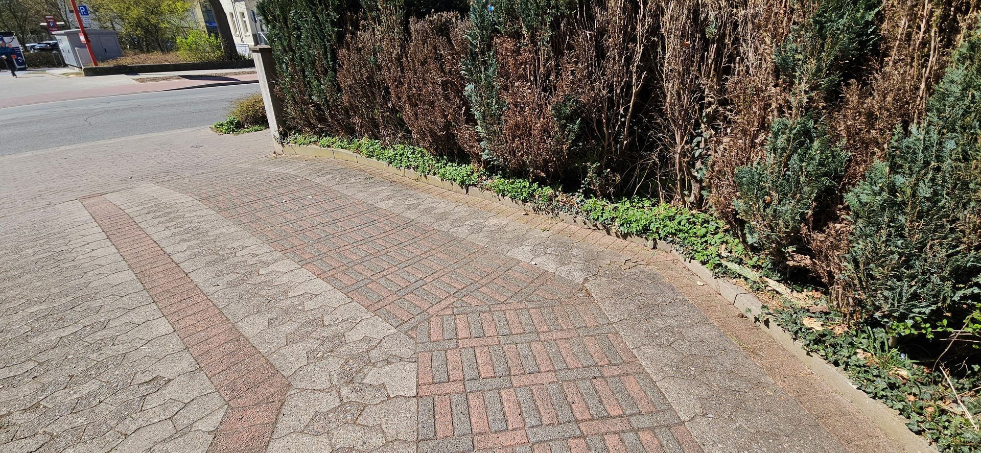 Ein gemauerter Weg, der zu einer Hecke am Straßenrand führt