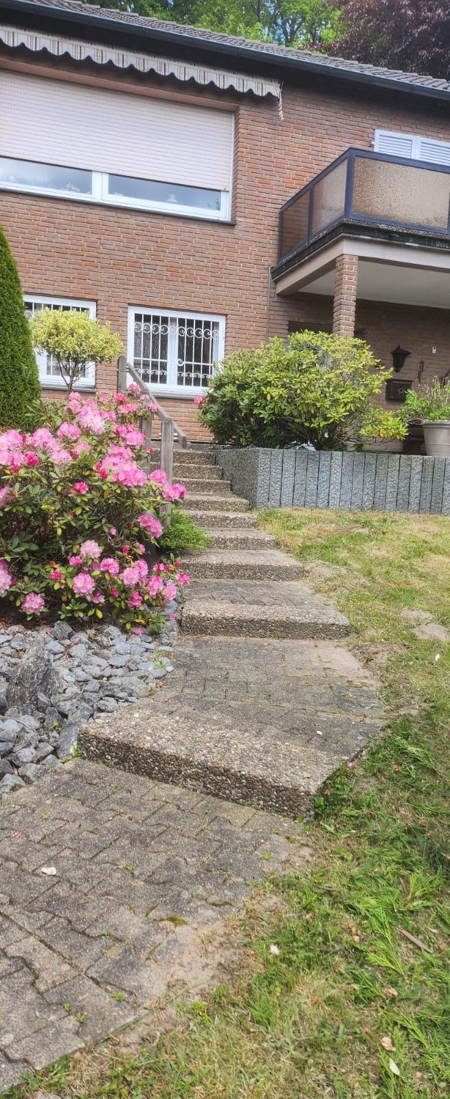 Ein Backsteinhaus mit einer Treppe nach oben und Blumen davor.