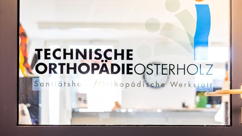 Eine Person zeigt auf ein Schild an einem Fenster mit der Aufschrift „Technische Orthopädieosterholz“.