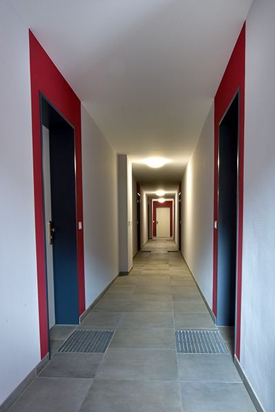 Langer Flur mit blauen, rot umrandeten Türen