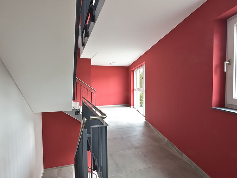 Flur mit roten Wänden, grauem Boden und weißer Decke.
