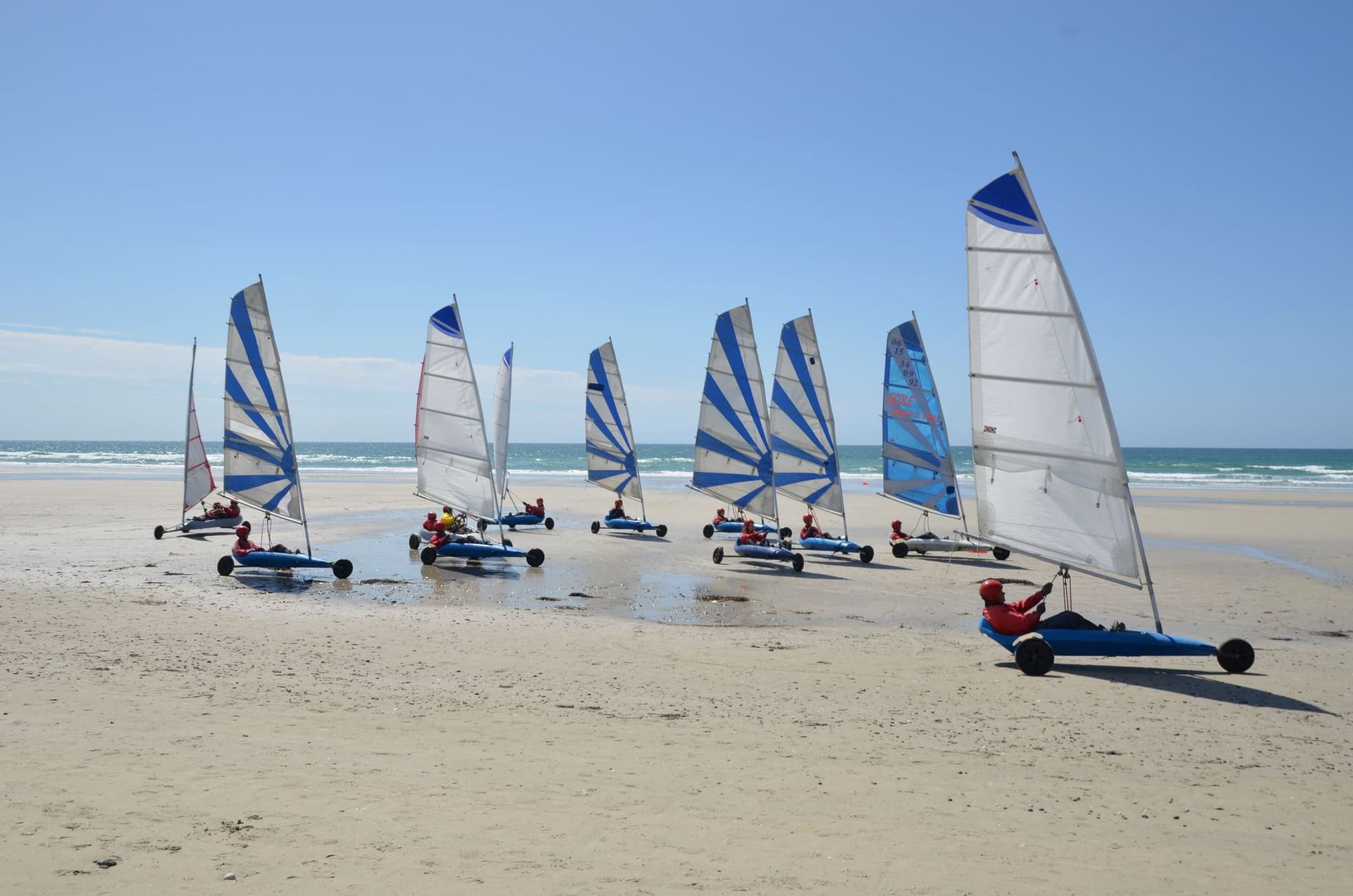 Des marins terrestres aux voiles colorées sur une plage de sable près de l'océan.