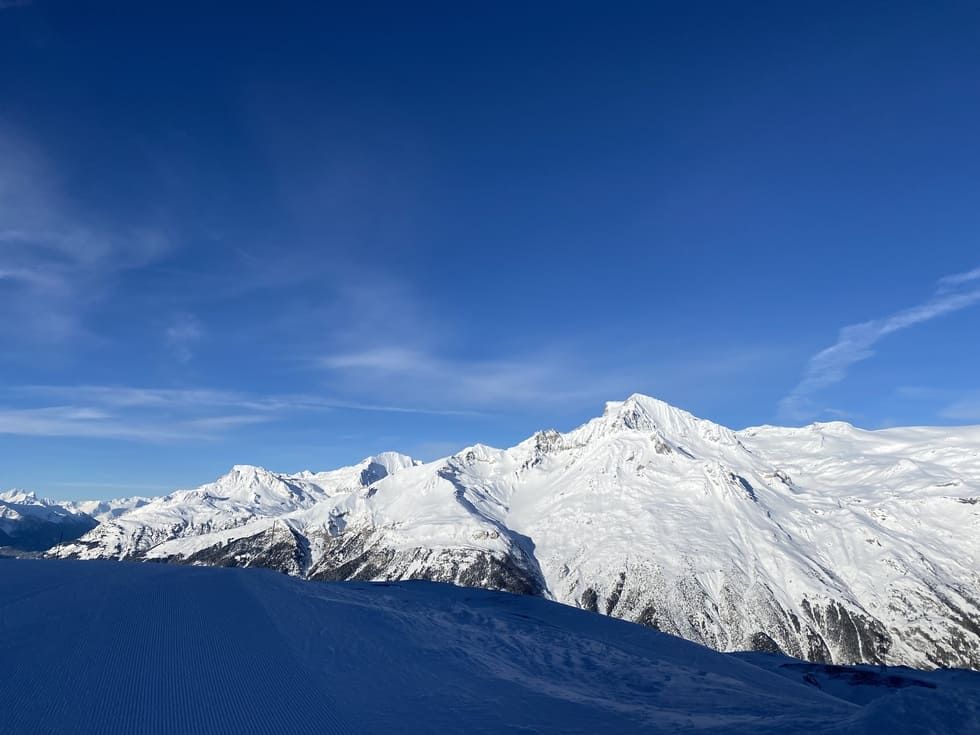 Montagnes enneigées sous un ciel bleu éclatant. Une pente enneigée est visible au premier plan.