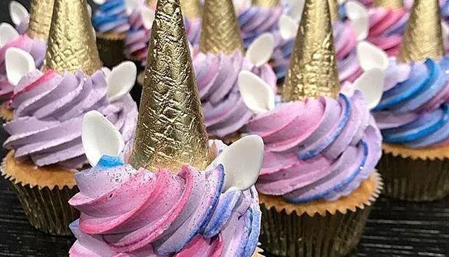 Un montón de cupcakes con cuernos de unicornio sobre una mesa.