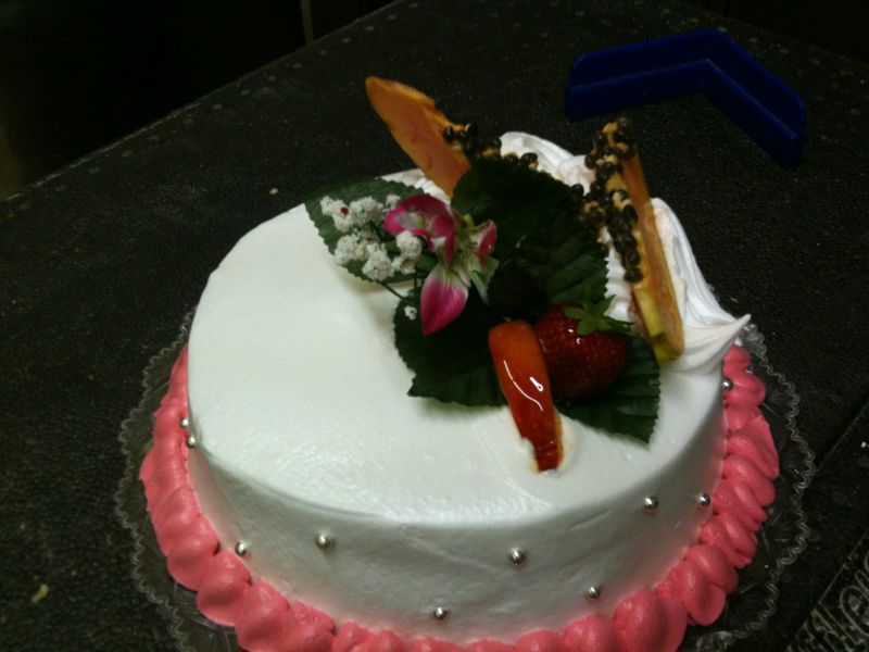 Un pastel blanco con glaseado rosa y fruta encima.