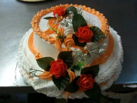 Un pastel blanco con glaseado de naranja y flores encima.