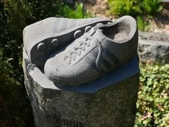 Eine graue Turnschuh-Skulptur, die im Freien auf einem Baumstumpf thront.