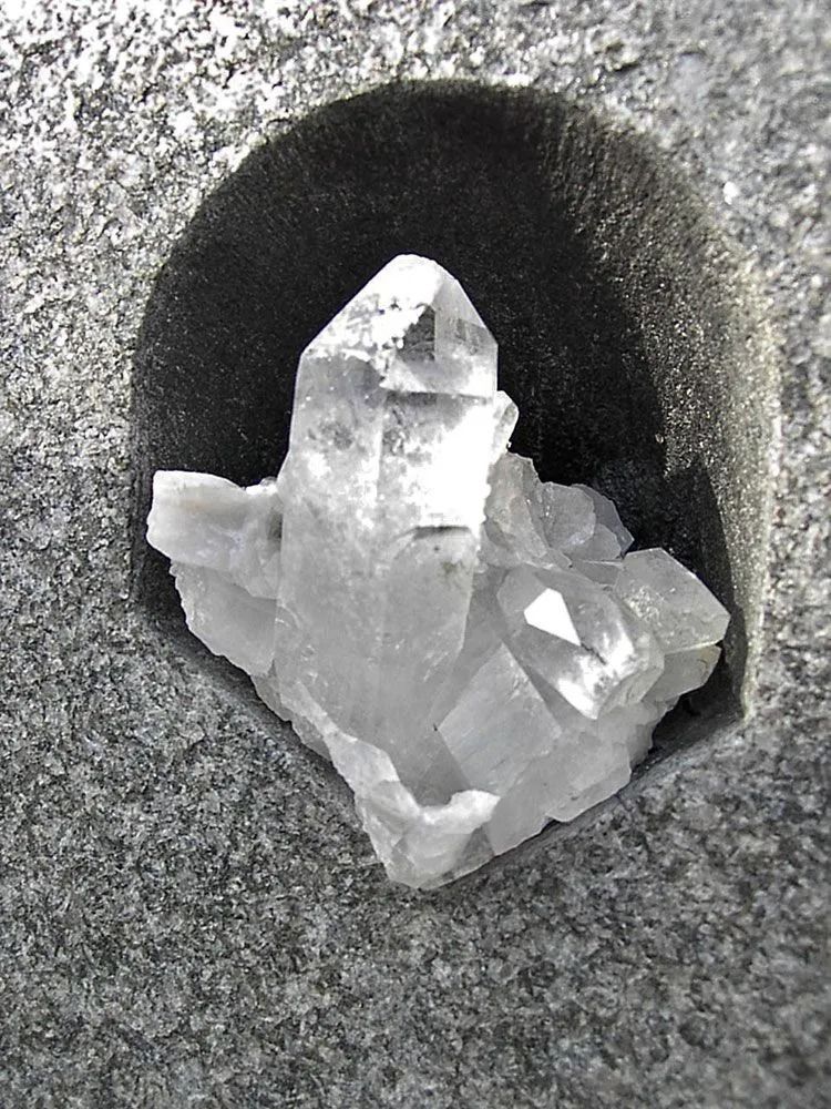 Klarer Quarzkristallcluster in einer kleinen, rauen Öffnung in grauem Gestein