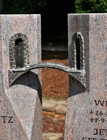 Ein in zwei Hälften geteiltes Steindenkmal, die durch eine gebogene Metallbrücke verbunden sind.