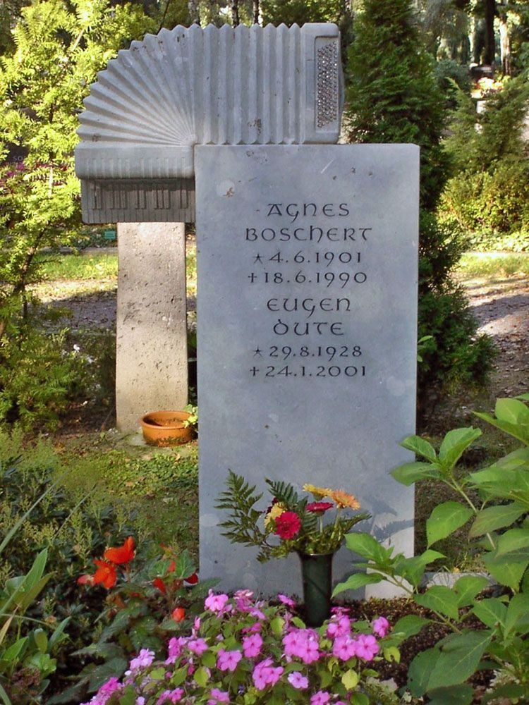 Grabstein in einem Garten mit Blumen und Grünpflanzen, mit der Inschrift „Eugen Boscher 1919–2001“.