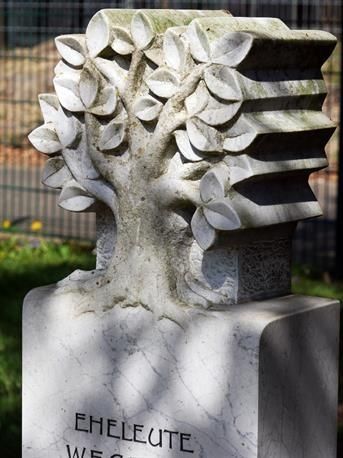 Gedenkskulptur aus weißem Stein mit abstrakten, baumartigen Blättern und eingraviertem Text auf dem Sockel