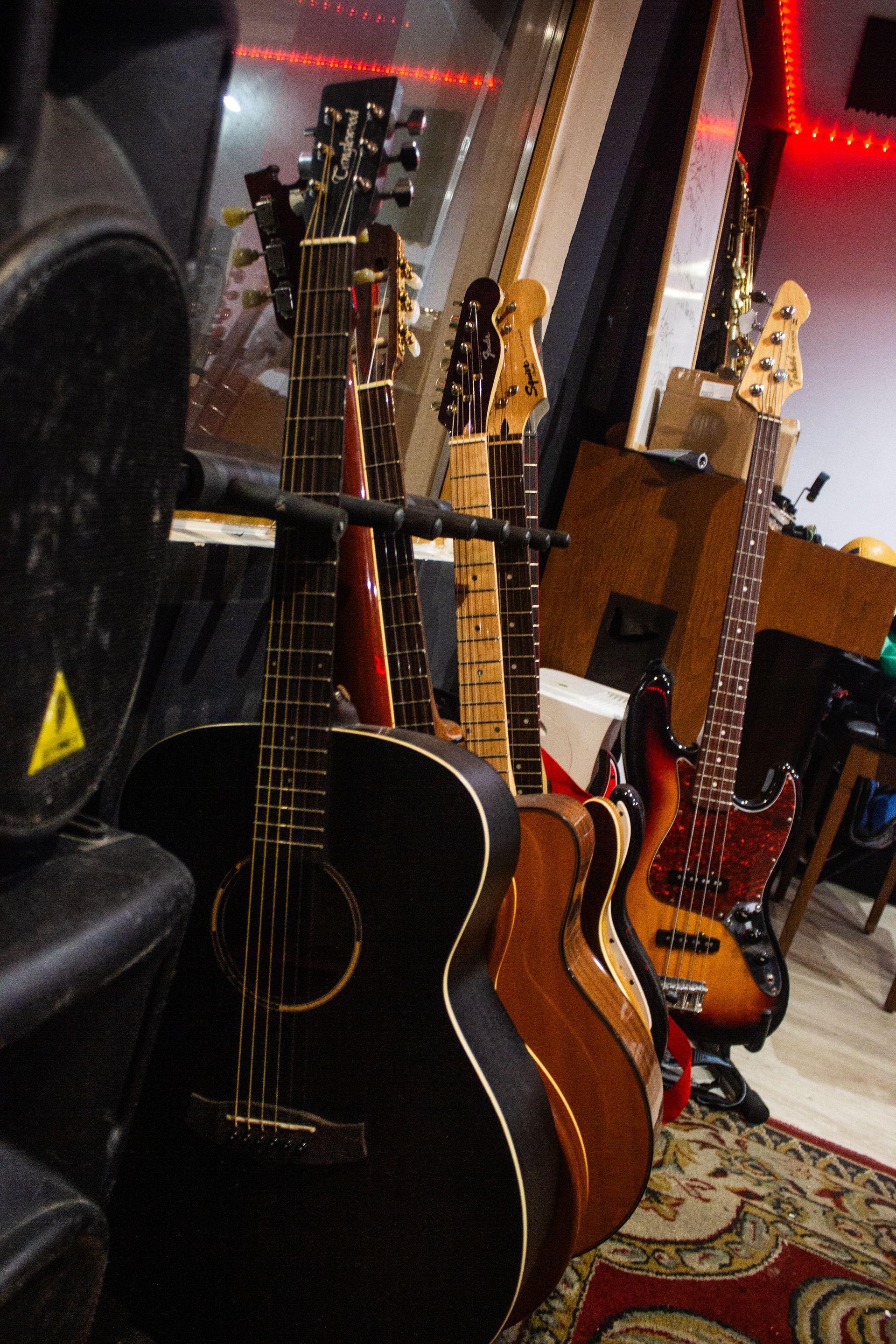 Varias guitarras y un bajo en una habitación. Destaca una guitarra acústica negra, cerca de un altavoz.