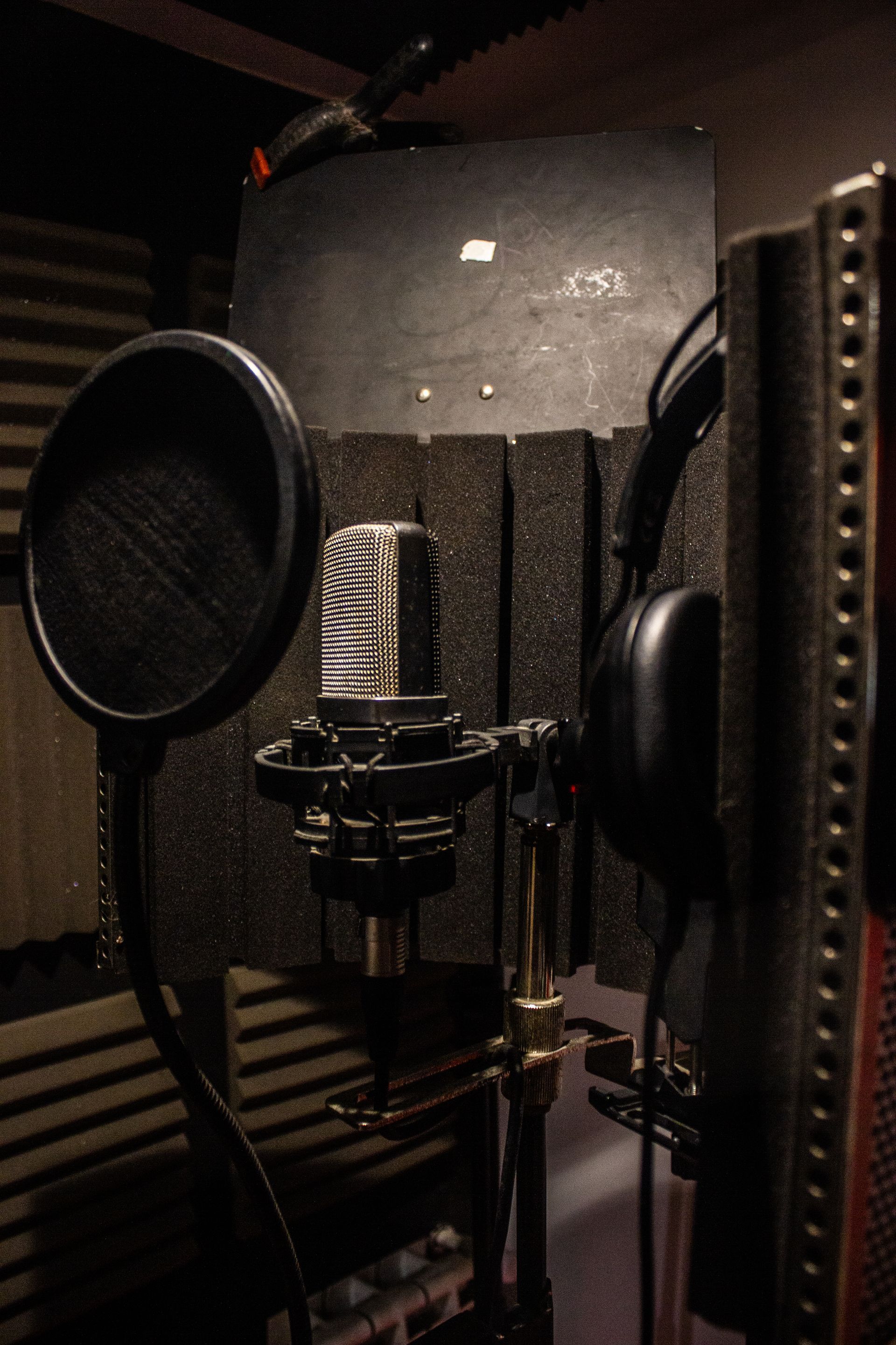 Micrófono, filtro antipop y auriculares en una cabina de grabación vocal insonorizada.