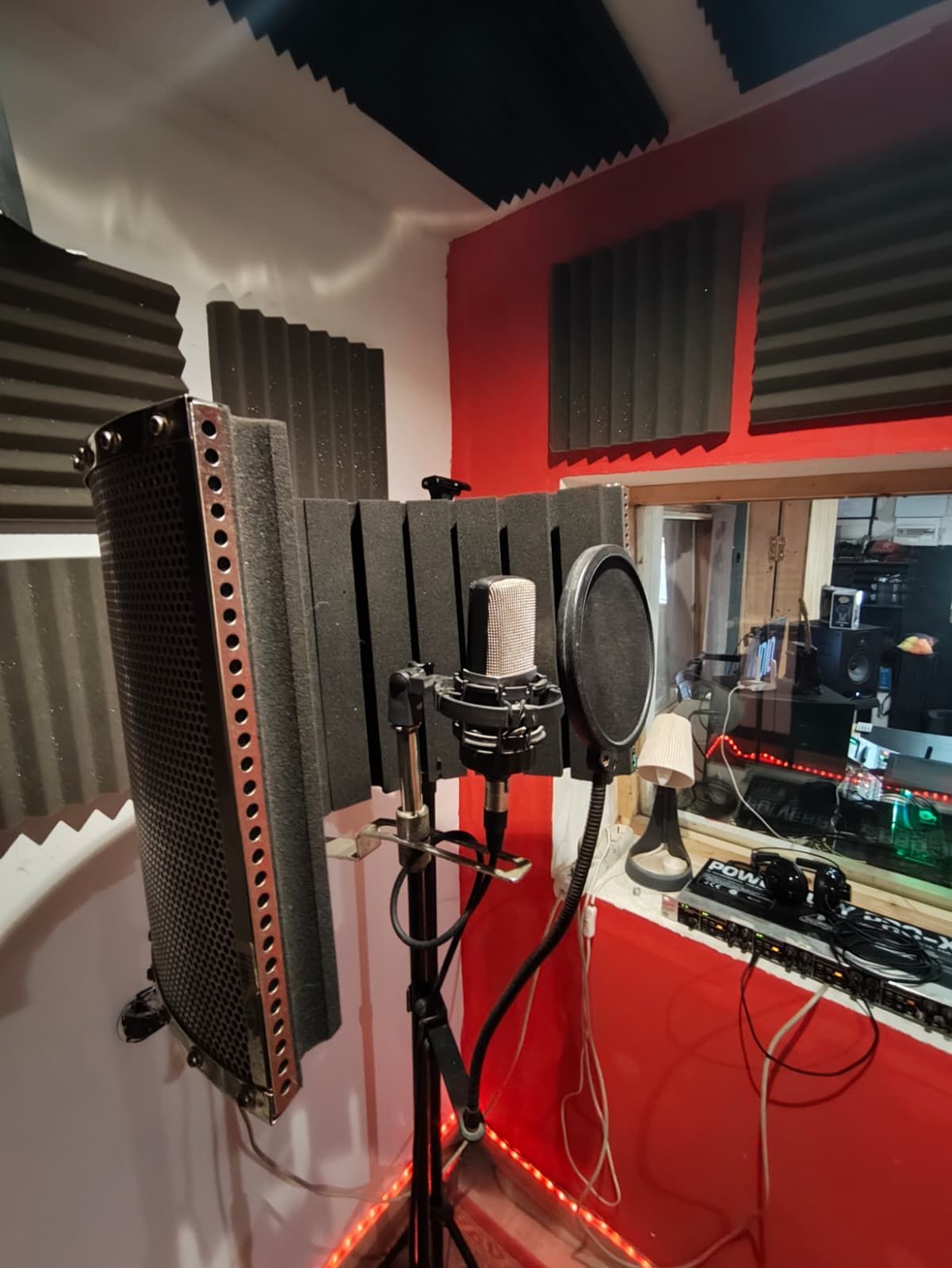 Configuración de micrófonos en un estudio de grabación de paredes rojas. Paneles de espuma acústica y cabina vocal.