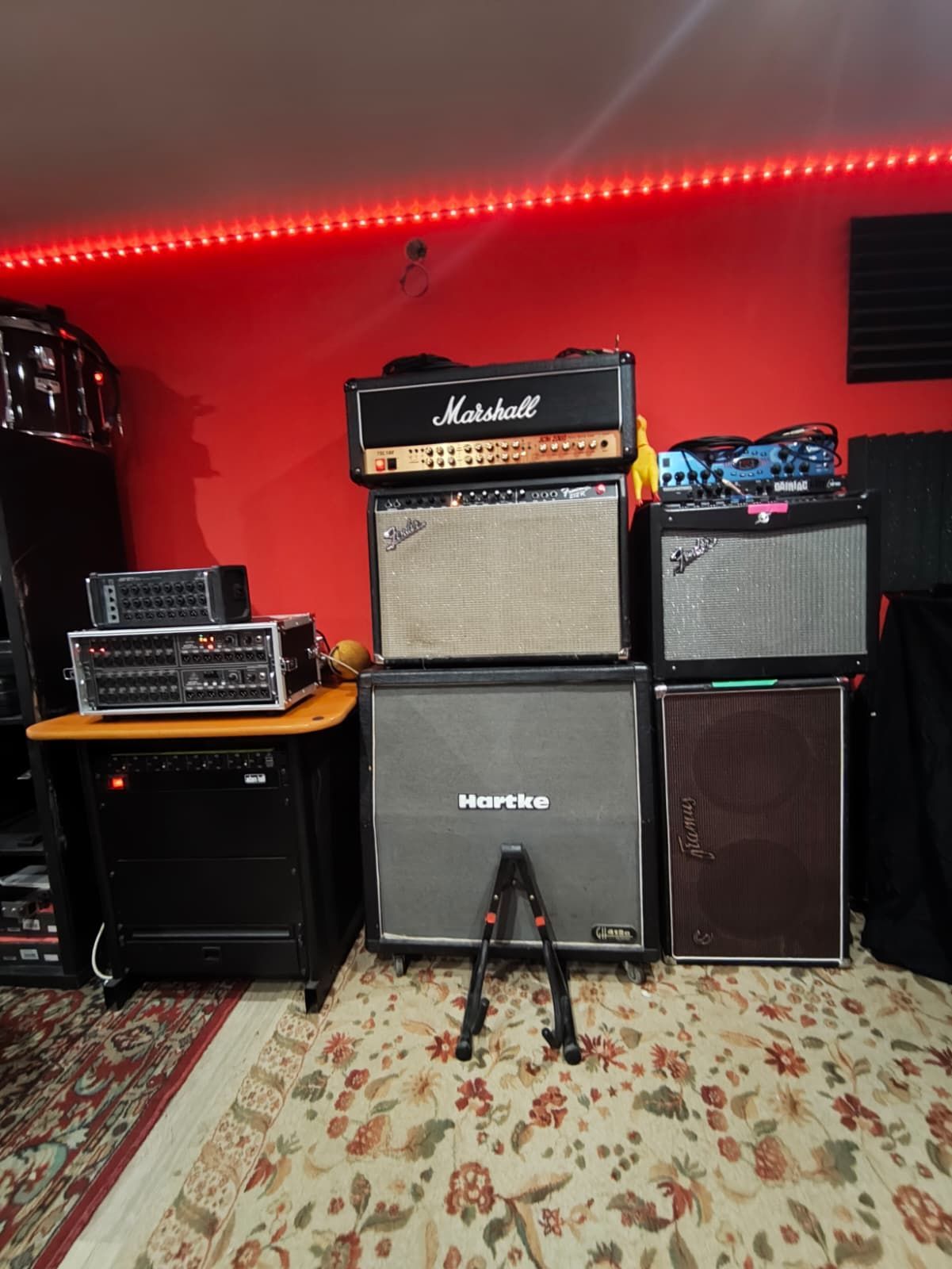 Colección de amplificadores en una habitación de paredes rojas con una tira de LED roja. Un cabezal Marshall descansa